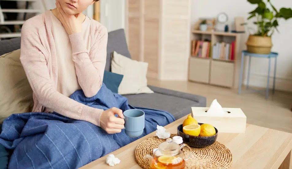 A woman holding a warm cup of tea while taking care of an inflamed or sore throat.